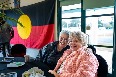 Two smiling women in front of Aboriginal Flag